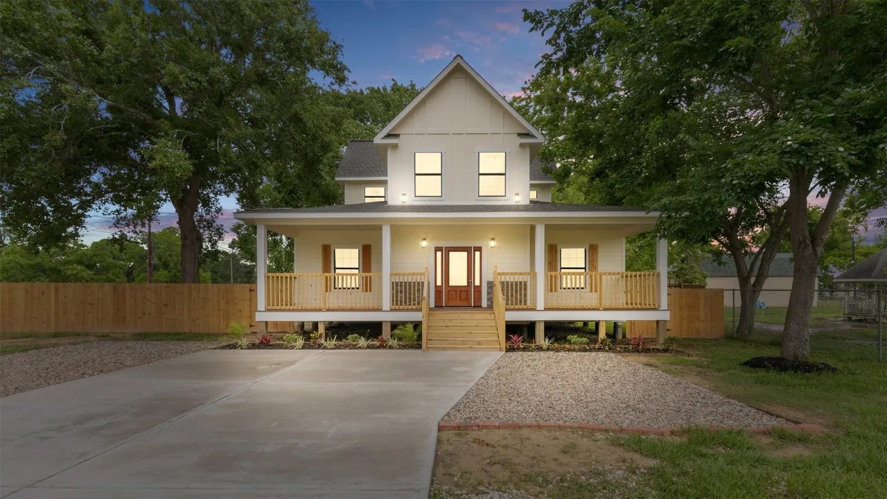 Front exterior at twilight — two-story farmhouse with lit covered wraparound porch