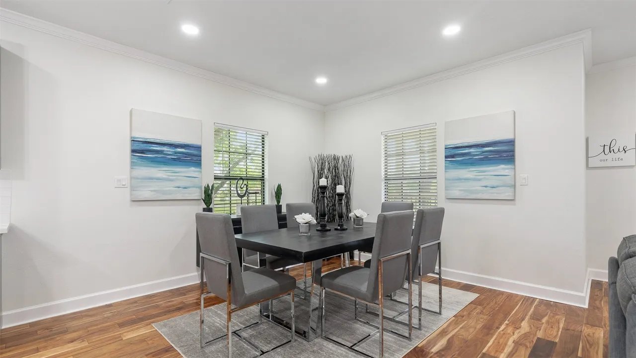 Formal dining area with bay-themed wall art, large windows, and engineered hardwood floors
