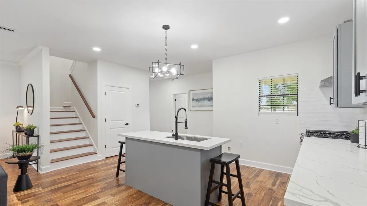 Kitchen island with stairwell behind — quartz waterfall, breakfast-bar seating, gooseneck faucet