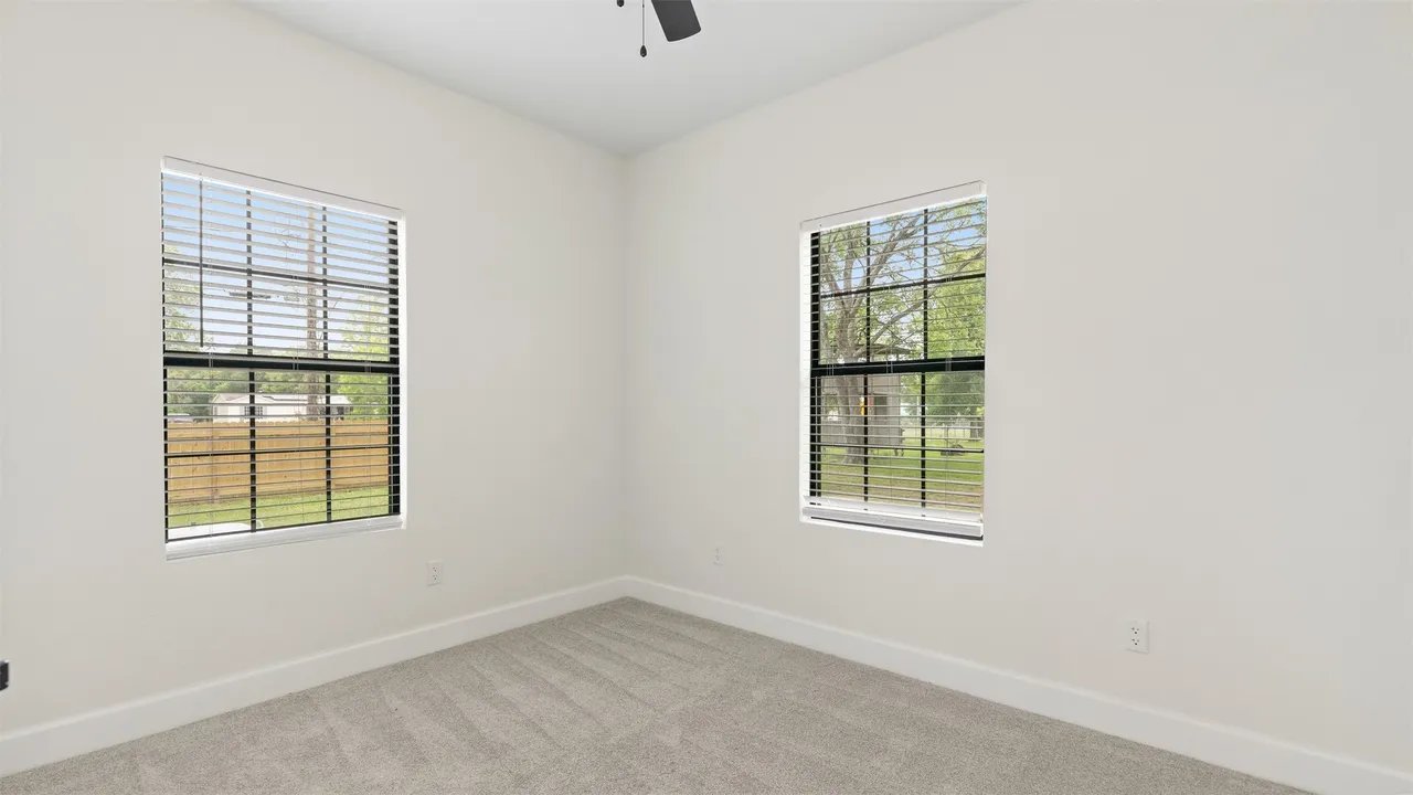 Upstairs bedroom with two windows, ceiling fan, plush carpet, and view of the fenced back yard