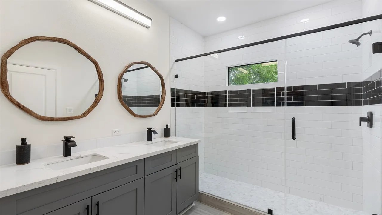 Primary bathroom with double vanity, wood-frame mirrors, and glass-enclosed walk-in shower
